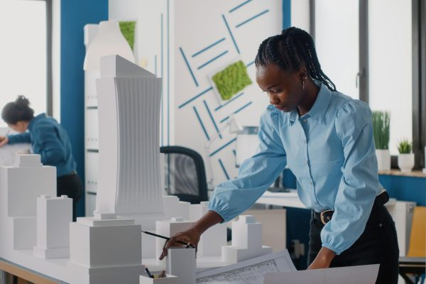african-american-woman-analyzing-blueprints-plan-building-model-work-architecture-architect-working-with-maquette-layout-print-design-urban-construction-development