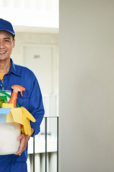 cheerful-asian-male-janitor-walking-into-hotel-room-carrying-supplies-bucket