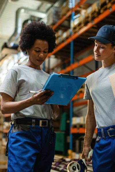 low-angle-view-two-female-workers-reading-delivery-schedule-list-while-working-distribution-warehouse